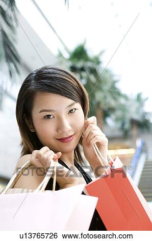 Stock Photograph - Young woman raising her shopping bags under her chin. Fotosearch