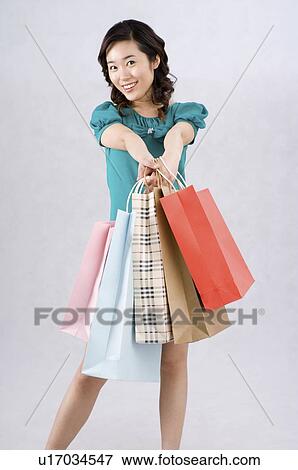 Stock Photo - Young woman raising shopping bags in front. Fotosearch