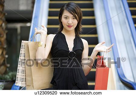 Stock Image - Young woman raising shopping bags on both sides. Fotosearch
