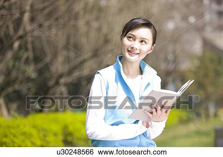 Stock Photograph - Young woman holding book outdoors. Fotosearch
