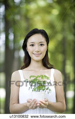 Stock Image - Young woman holding potted plant. Fotosearch