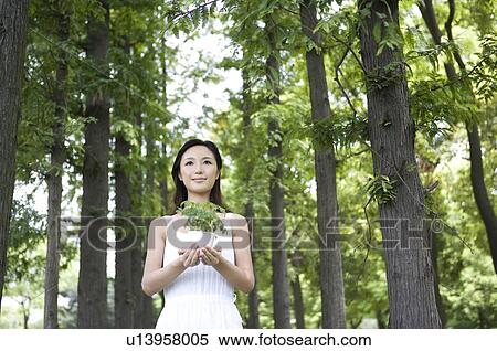 Stock Photography - Young woman holding potted plant outdoors. Fotosearch