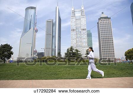 Picture - Young woman jogging, buildings in the background. Fotosearch