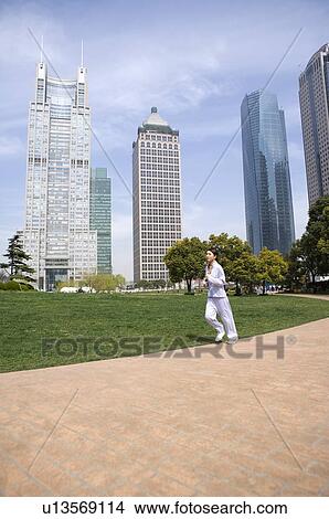 Young woman jogging in park, buildings in the background View Large Photo Image Picture - Young woman jogging in park, buildings in the background. Fotosearch