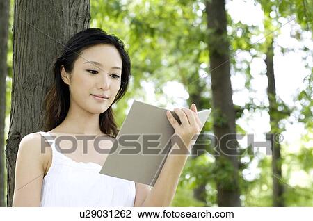 Young woman leaning against tree reading book View Large Photo Image Stock Image - Young woman leaning against tree reading book. Fotosearch