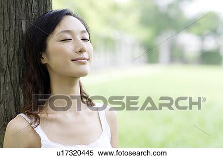 Stock Photography - Young woman leaning on tree. Fotosearch
