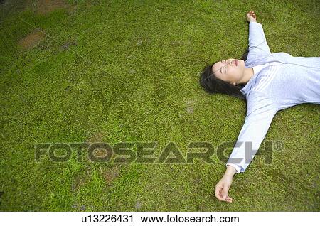 Stock Image - Young woman lying on lawn, eyes closed. Fotosearch