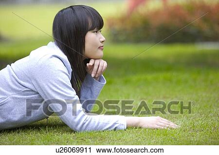 Stock Image - Young woman lying on lawn looking at distance. Fotosearch