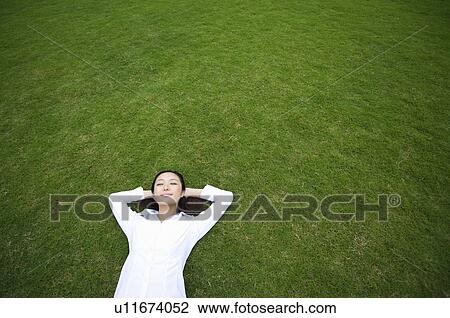 Stock Image - Young woman lying on lawn. Fotosearch