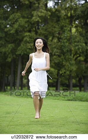 Stock Image - Young woman running on lawn. Fotosearch