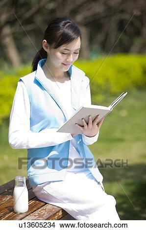 Picture - Young woman sitting on bench reading book. Fotosearch