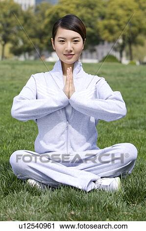 Stock Image - Young woman sitting on lawn in prayer position. Fotosearch