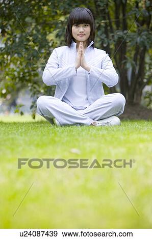 Stock Photo - Young woman sitting on lawn in prayer position. Fotosearch