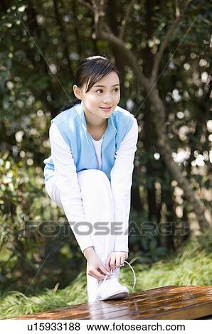 Stock Photo - Young woman tying laces on bench. Fotosearch