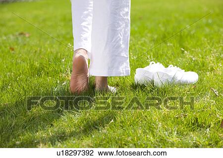Stock Image - Young woman walking barefoot on the lawn. Fotosearch