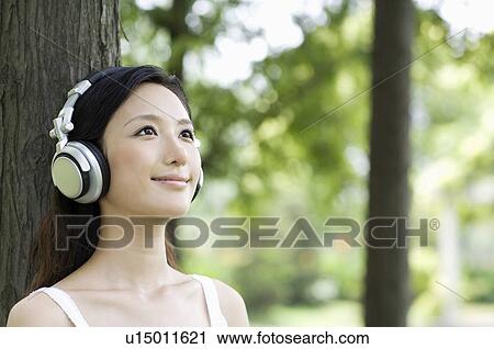 Young woman wearing headphone leaning against tree View Large Photo Image Stock Image - Young woman wearing headphone leaning against tree. Fotosearch