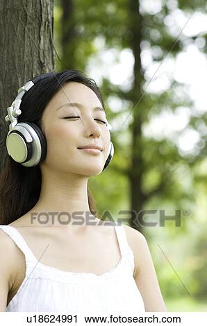 Young woman wearing headphones leaning on tree View Large Photo Image Stock Image - Young woman wearing headphones leaning on tree. Fotosearch