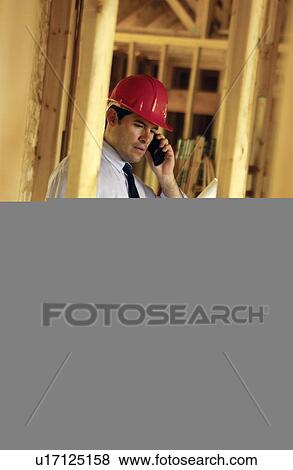 Contractor on cell phone looking over blueprints View Large Photo Image Stock Photo - Contractor on cell phone looking over blueprints. Fotosearch