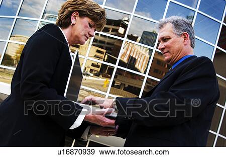 Stock Photo - Businessman using laptop businesswoman is holding. Fotosearch