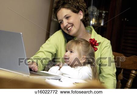 Mom working at home while holding daughter View Large Photo Image Stock Image - Mom working at home while holding daughter. Fotosearch