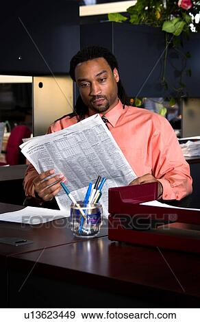 Stock Photo - African American businessman reading newspaper at his desk. Fotosearch