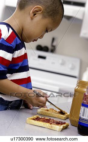 Stock Image - Asian boy fixing peanut butter and jelly sandwich. Fotosearch