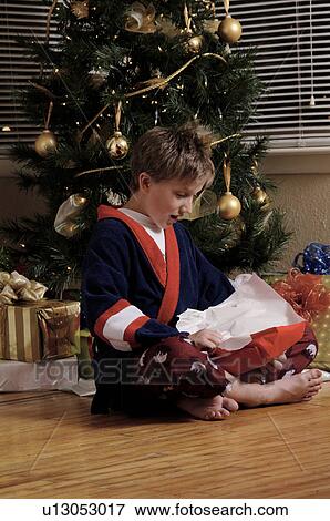 Boy near Christmas tree opening gifts View Large Photo Image Stock Photo - Boy near Christmas tree opening gifts. Fotosearch
