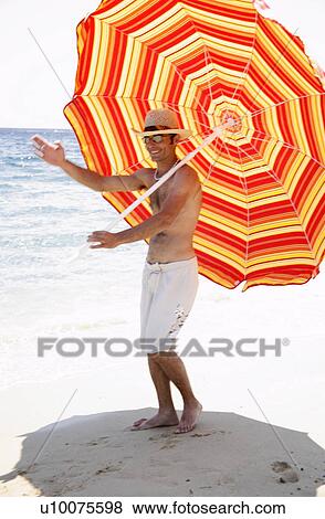 Stock Photo - Man marching on beach with beach umbrella. Fotosearch