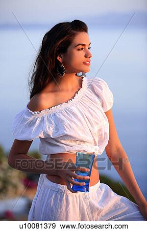 Stock Photo - Woman in white outfit on terrace with a view. Fotosearch