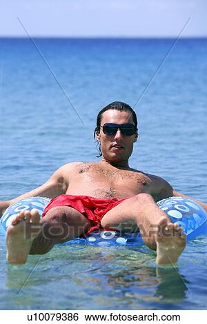 Young man in water on inflatable life ring View Large Photo Image Stock Photograph - Young man in water on inflatable life ring. Fotosearch