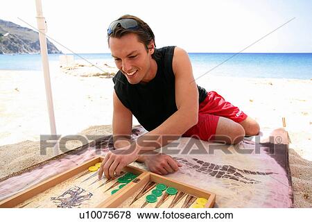 Stock Photo - Young man on beach playing backgammon. Fotosearch