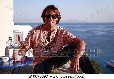 Stock Photo - Young man sitting on balcony with a view. Fotosearch