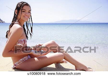 Young woman in bikini on beach holding shells View Large Photo Image Stock Photo - Young woman in bikini on beach holding shells. Fotosearch