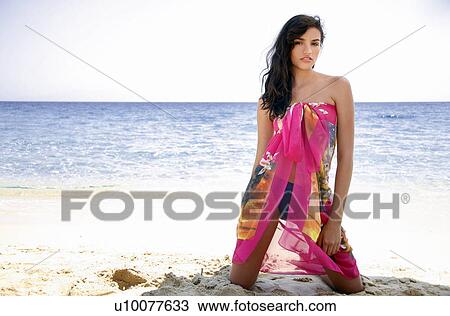 Stock Image - Young woman kneeling on beach. Fotosearch