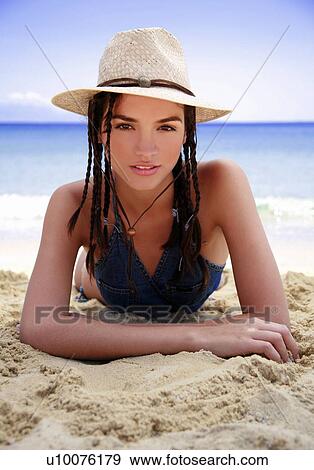 Stock Photo - Young woman lying on beach with hat. Fotosearch