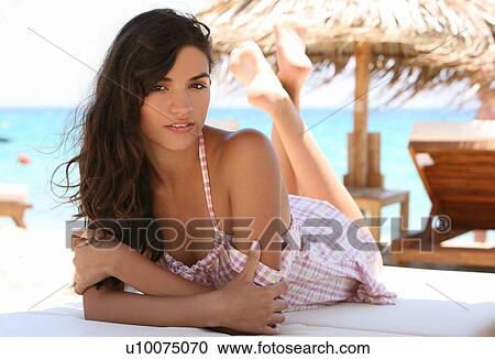 Stock Image - Young woman on chaise lounge on beach. Fotosearch