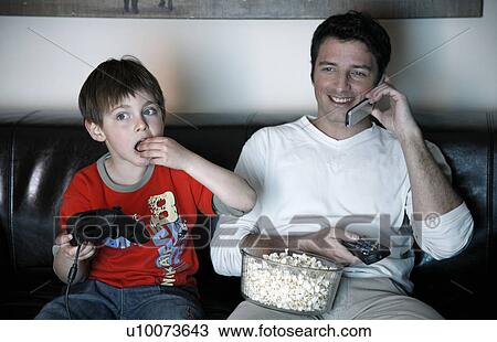 Father talking on cell phone while boy is playing a video game View Large Photo Image Stock Image - Father talking on cell phone while boy is playing a video game. Fotosearch