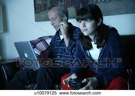 Stock Photography - Grandfather works on laptop while granddaughter plays video game. Fotosearch