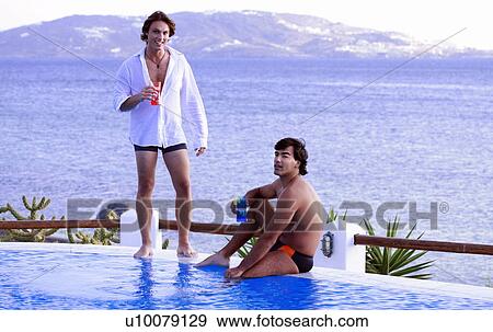 Stock Photo - Two men with cocktails at a seaside pool. Fotosearch
