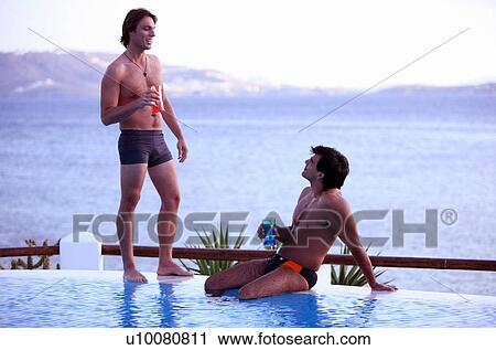 Stock Image - Two men with cocktails by the poolside. Fotosearch