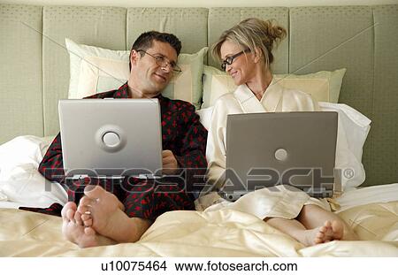Picture - Mature couple working in bed. Fotosearch