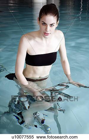 Stock Photography - Young woman on exercise bike in spa pool. Fotosearch