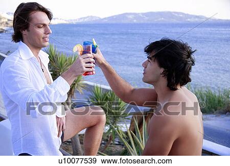 Stock Photo - Two men toasting with cocktails by the seaside. Fotosearch