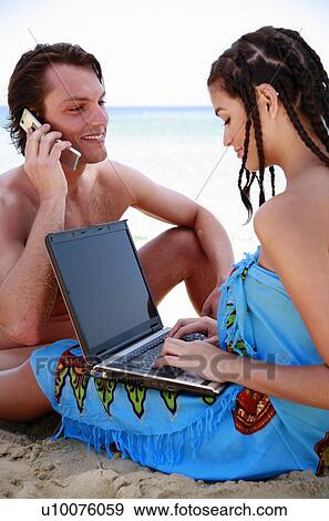 Stock Photo - Young couple on beach with laptop and cell phone. Fotosearch