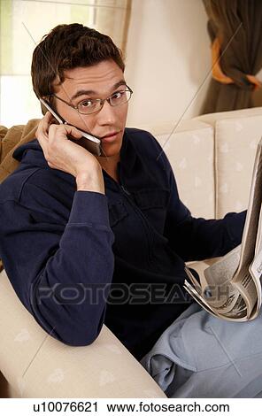 Young man reading newspaper and talking on cell phone View Large Photo Image Stock Image - Young man reading newspaper and talking on cell phone. Fotosearch