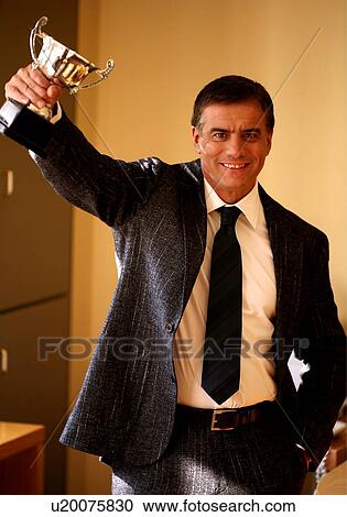 Stock Image - Businessman holding trophy. Fotosearch
