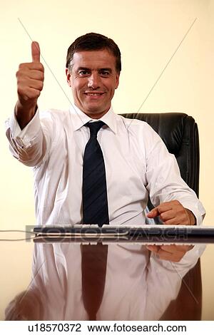 Businessman sitting at desk and making a thumbs up gesture View Large Photo Image Stock Image - Businessman sitting at desk and making a thumbs up gesture. Fotosearch
