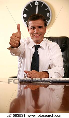 Businessman sitting at desk and making a thumbs up gesture View Large Photo Image Stock Image - Businessman sitting at desk and making a thumbs up gesture. Fotosearch