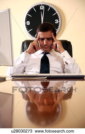 Stock Image - Businessman sitting at his desk lost in thought. Fotosearch