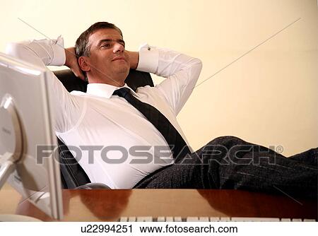 Businessman sitting at his desk with hands behind his head View Large Photo Image Stock Image - Businessman sitting at his desk with hands behind his head. Fotosearch